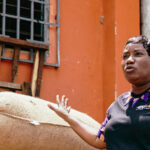 Doumbia Assata Kone steht vor Säcken mit Kakaobohnen.